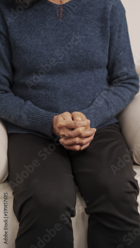Asian mature woman feels nervous anxious or lonely put clenched hands on laps sitting on couch, sitting on sofa.