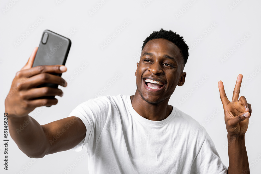 Close up shot selective focus happy emotional african american black man holding new modern last series smartphone in hands taking photo selfie showing two fingers at camera. Close up shot selective focus happy emotional african american black man holding new modern last series smartphone in hands taking photo selfie showing two fingers at camera.
