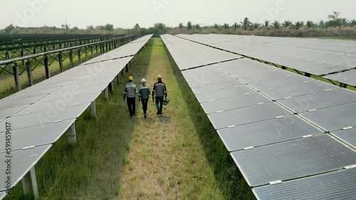 Top aerial view of Engineers checking a Solar Panels and walking in solar farm. engineers inspects construction of solar cell panel. Drone flight fly over solar panels field renewable green energy.