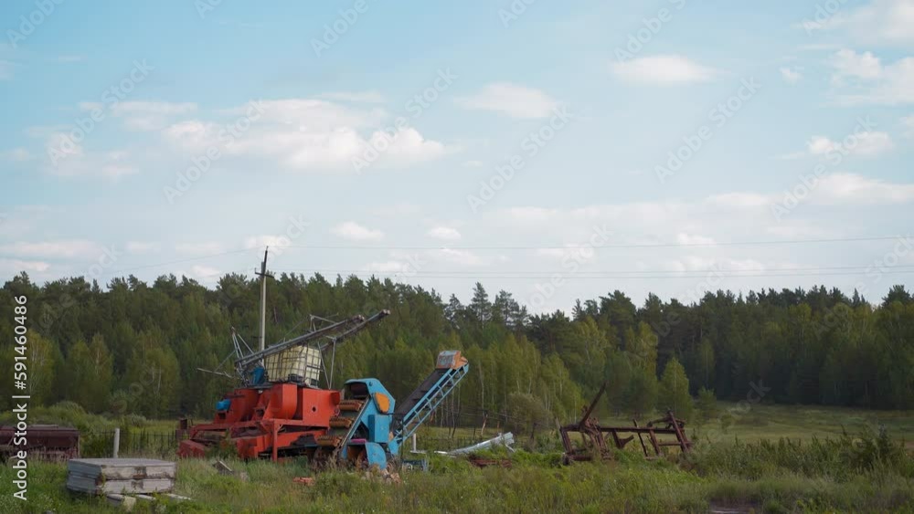 Old agricultural machines parts in field at summer countryside. Abandoned farming equipment against green forest. Landscape with industrial elements Old agricultural machines parts in field at summer countryside. Abandoned farming equipment against green forest. Landscape with industrial elements