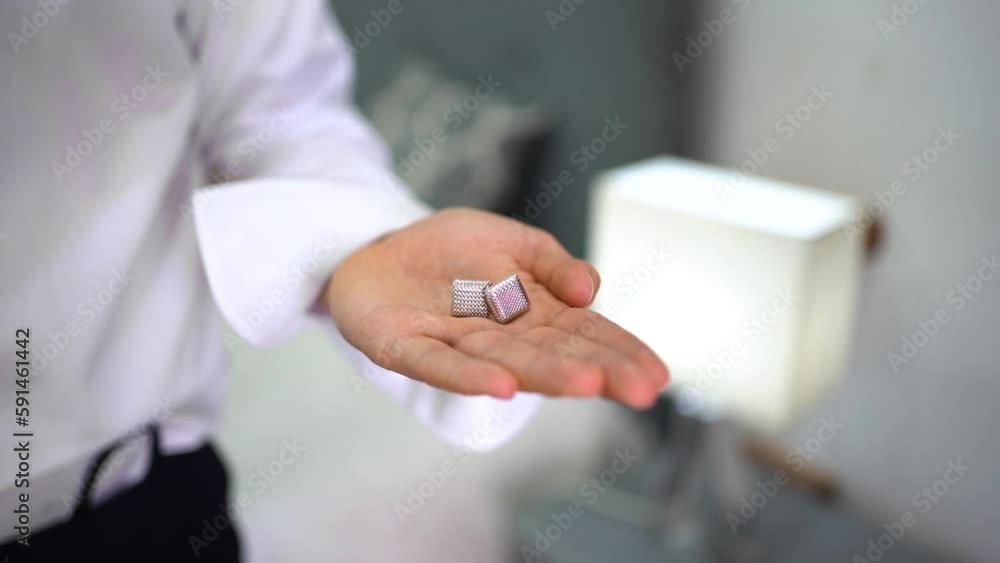 Groom holding in his hand a pink cufflinks on wedding morning, Orbiting shot Groom holding in his hand a pink cufflinks on wedding morning, Orbiting shot
