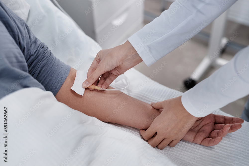 Close-up of doctor putting an IV drip to patient intravenously while she lying on bed in hospital ward Close-up of doctor putting an IV drip to patient intravenously while she lying on bed in hospital ward