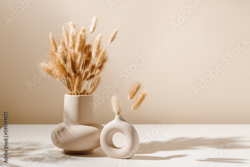 Stylish ceramic vase set on the table with dried lagurus grass bouquet with shadows, light brown wall background. Scandinavian vase on the table with copy space, minimal aesthetic interior decoration