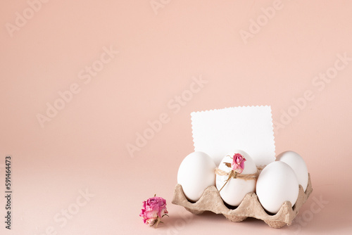 Fototapeta Naklejka Na Ścianę i Meble -  A mock-up of an invitation with Easter eggs and an eco-decor of dried roses and a wooden rabbit on a beige background. happy Easter