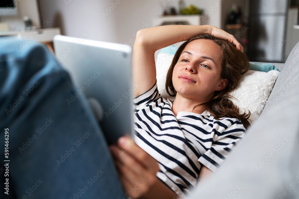 Young woman uses her digital tablet while relaxing at home lying on sofa. Young woman uses her digital tablet while relaxing at home lying on sofa.