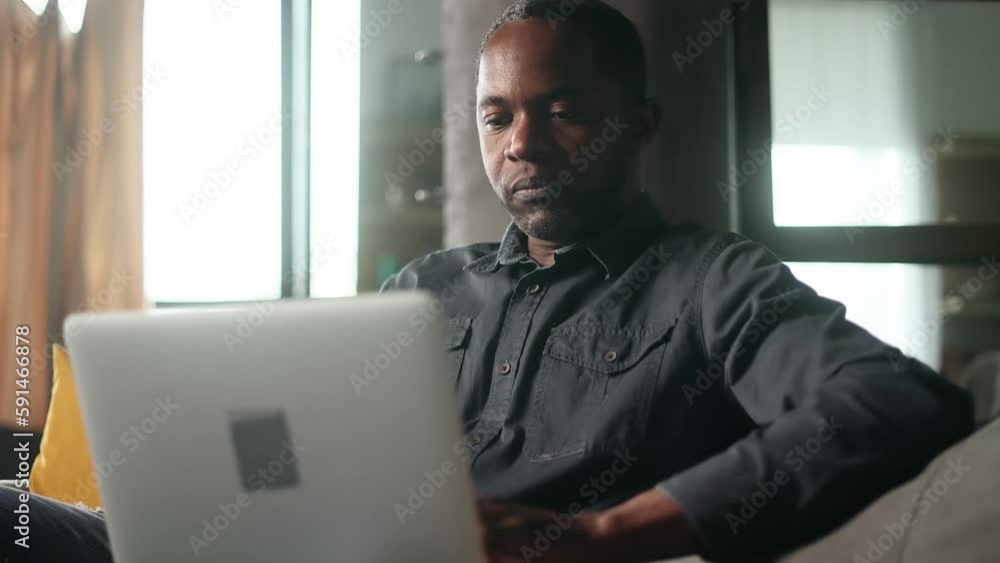 Portrait of mature african american man relaxing at home or working online typing browsing products in internet store checking email or social media profile on laptop computer and eating pizza indoors Portrait of mature african american man relaxing at home or working online typing browsing products in internet store checking email or social media profile on laptop computer and eating pizza indoors