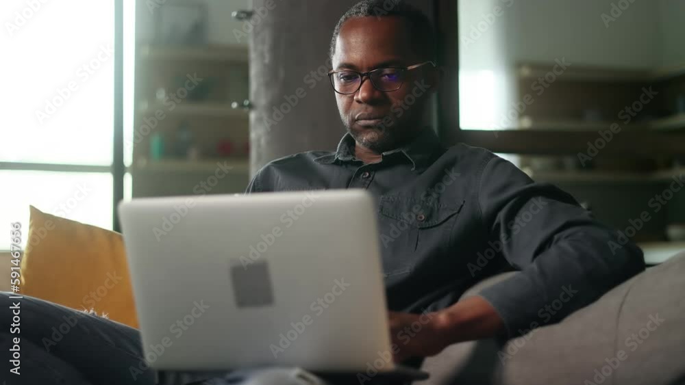 Portrait of mature african american man with glasses relaxing at home or working online typing browsing products in internet store checking email or social media profile on laptop computer indoors Portrait of mature african american man with glasses relaxing at home or working online typing browsing products in internet store checking email or social media profile on laptop computer indoors