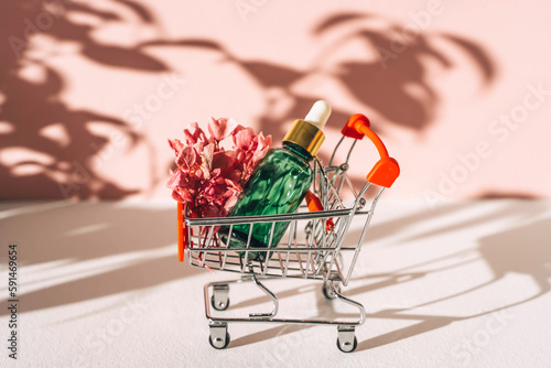 Face serum in shopping cart on pink background. photo