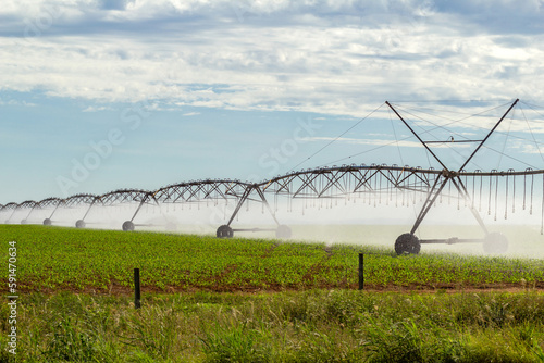Máquina de irrigação molhando a plantação que está crescendo, em um dia claro com algumas nuvens no céu.
