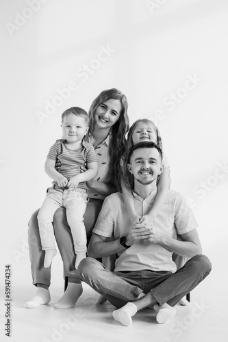 Young happy mother, father embrace child daughter and son isolated in background studio. Parents hug children relaxing on a sofa on a wall at home. Family moving into new house. Black and white photo.