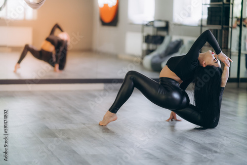 a charming girl in black sportswear, sitting on a longitudinal splits. Good stretching and gymnastics