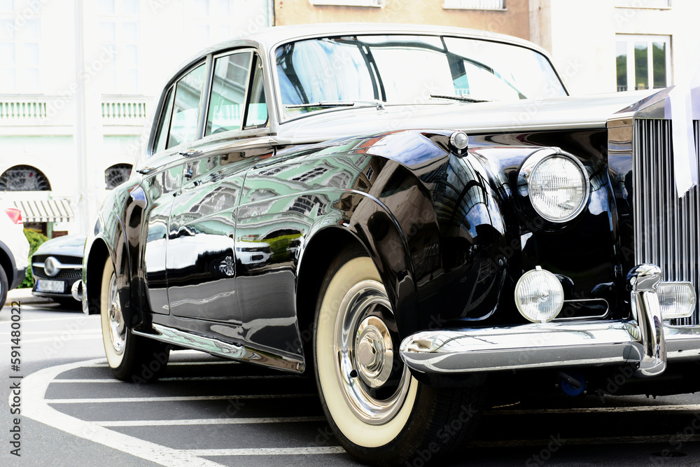classic old British made elegant and expensive car closeup. headlights and shiny side panel. white walled rubber tires. wedding and marriage concept. ribbon on front grille. soft blurred background. 