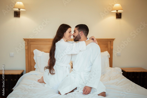 Loving Husband And Wife Embracing Sitting On Bed At Home