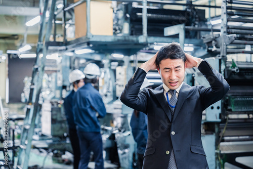 工場で頭を抱えるスーツの男性 © maroke