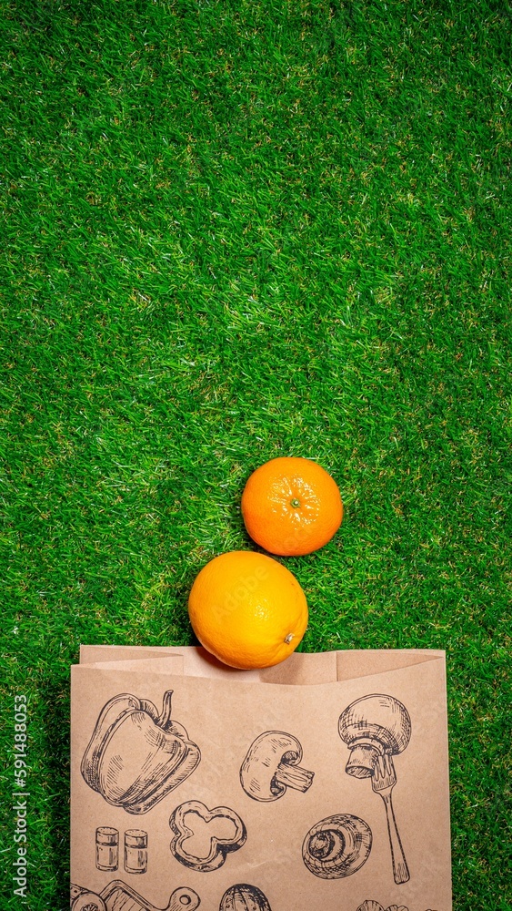 Naklejka premium Banana, red apple and different fruits with craft paper bag laying on grass, flat lay. Space for text. Zero waste concept.