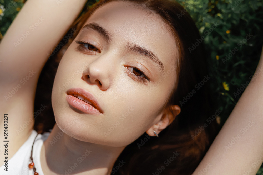 Fototapeta premium Top view of young woman looking at camera while lying on meadow.