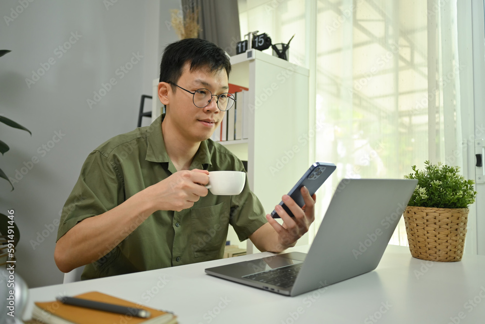 Image of man in glasses drinking hot coffee and texting messages, chatting in social on smartphone Image of man in glasses drinking hot coffee and texting messages, chatting in social on smartphone