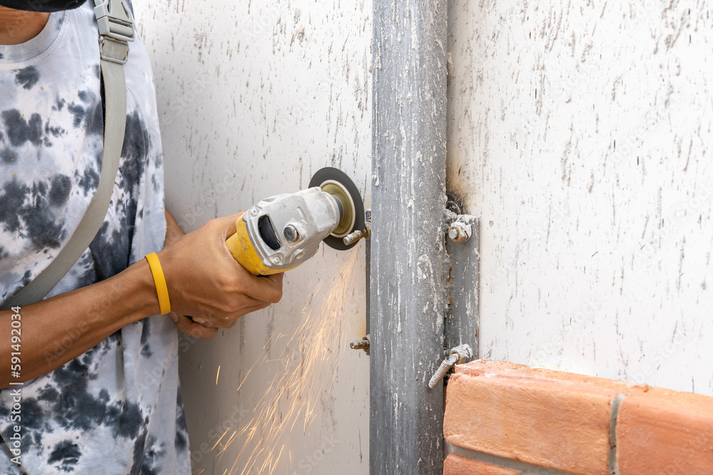 Asian worker young man sawing and kept detailed metal screw from a steel pole for preparing to install foam brick wall.