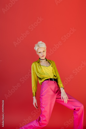 blonde woman with bright eyeliner posing in trendy outfit on carmine pink background.