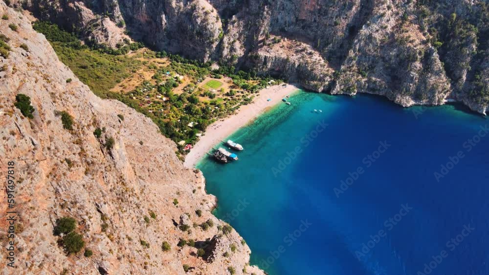 Drone video capturing the pristine Butterfly Valley in Ölüdeniz, Fethiye, featuring its tranquil beach, canyon, waterfall, and boats cruising along the vibrant turquoise sea. Drone video capturing the pristine Butterfly Valley in Ölüdeniz, Fethiye, featuring its tranquil beach, canyon, waterfall, and boats cruising along the vibrant turquoise sea.