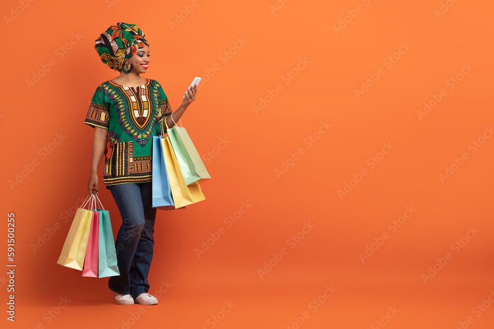 Happy african woman have shopping, using smartphone on orange