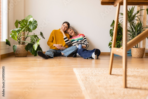 Smiling mother and daughter sitting on hardwood floor at home