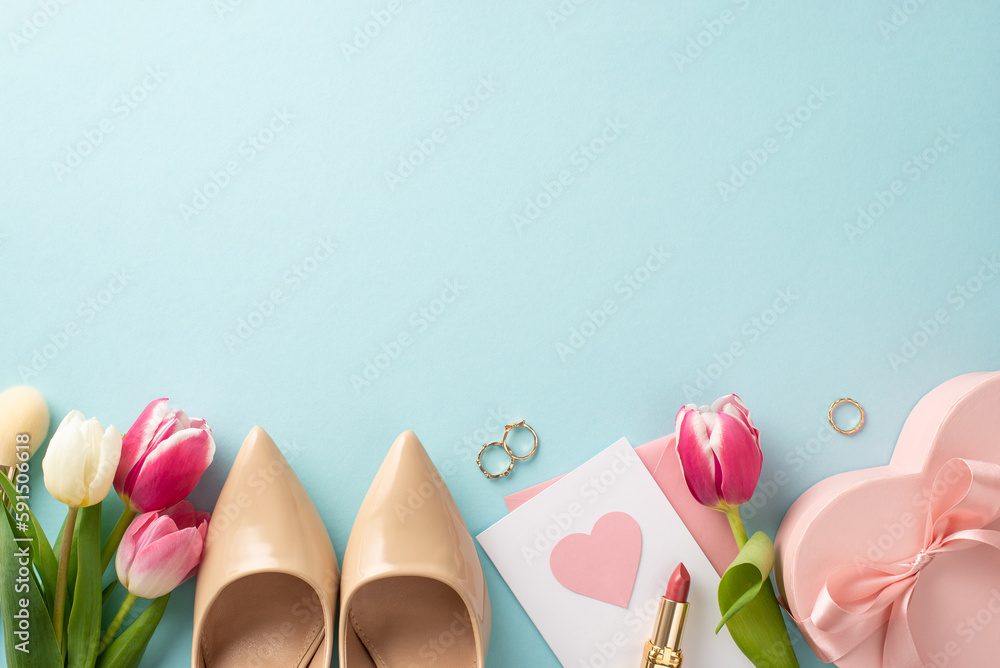 Beautiful Mother's Day concept. Top view flat lay of high-heels, present box, tulips, lipstick, postcard on pastel blue background with an area for text or advert