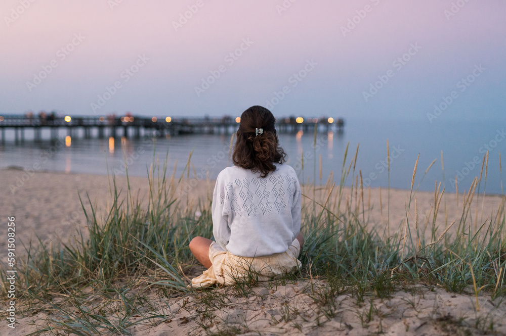 Frau am Strand bei Yoga am Strand mit Blick auf einen Steg in der Abenddämmerung