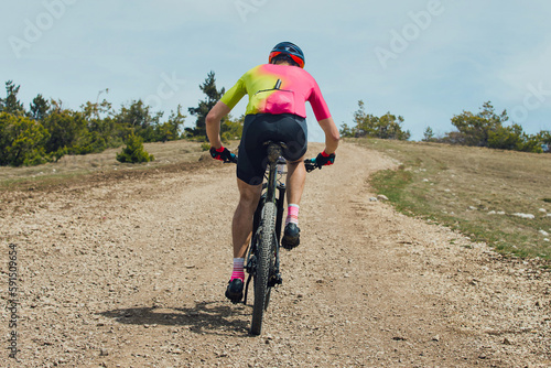 rear view athlete cyclist riding mountain bike uphill, biking on gravel road, cycling competition