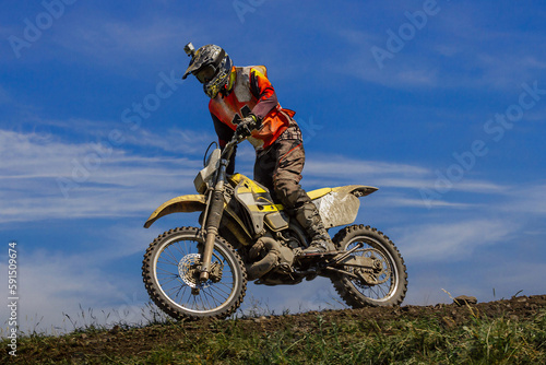 motocross rider riding off-road motorsport racing dusty trail on background blue sky