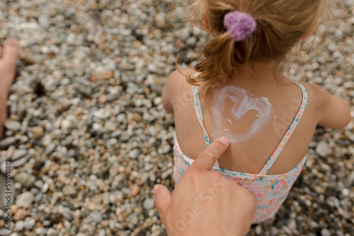 Man drawing heart shape with suntan lotion on daughter at beach photo