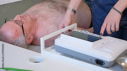A female cardiologist puts rubber vacuum electronic sensors on an elderly male patient's ECG photo