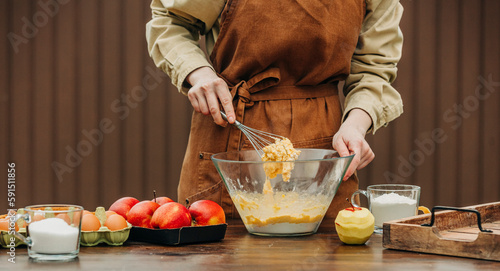 Woman in apron stirring cake dough in mixing bowl at table