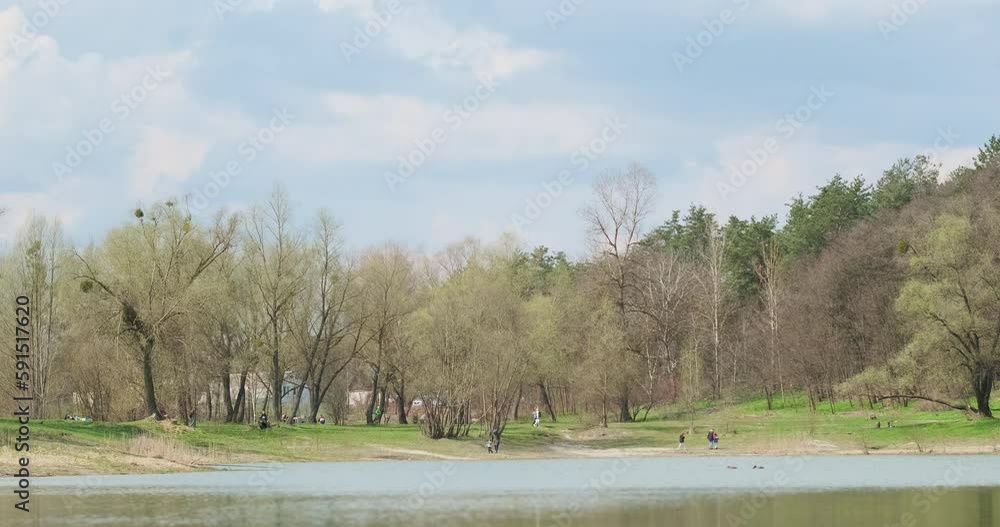 Spring landscape of city park with lake. People are walking along the shore, the sky is blue. Wide shot, nature, relaxation. Spring landscape of city park with lake. People are walking along the shore, the sky is blue. Wide shot, nature, relaxation.