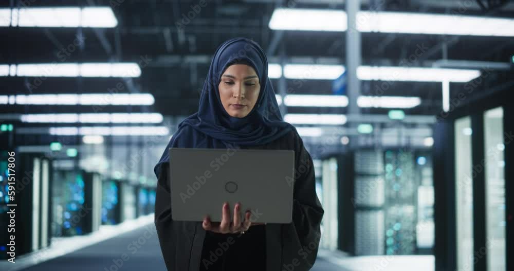 Portrait of a Young Middle Eastern Female IT System Engineer Wearing Traditional Hijab, Using Laptop Computer in a Modern Technological Server Facility. Arab Artificial Intelligence Expert at Work Portrait of a Young Middle Eastern Female IT System Engineer Wearing Traditional Hijab, Using Laptop Computer in a Modern Technological Server Facility. Arab Artificial Intelligence Expert at Work