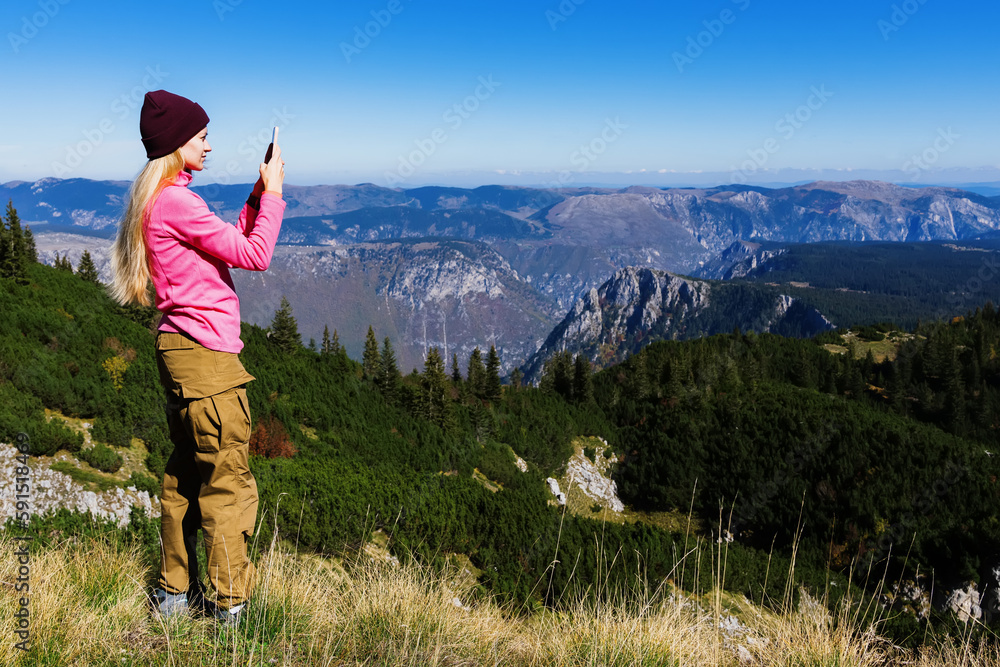 A young woman takes a photo of mountains while traveling. A tourist takes pictures of mountain ranges