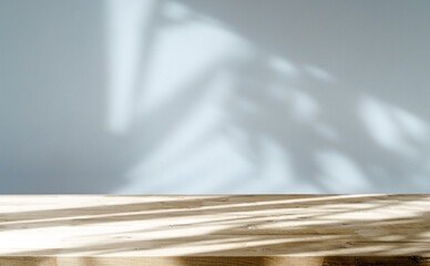 Table shadow background. Wooden table and white empty wall with plant shadows.
