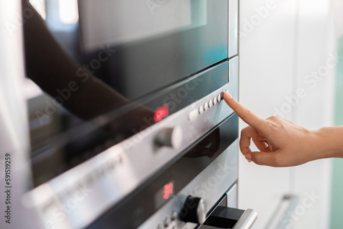 Woman Touching Control Panel On Electric Oven In Kicthen With Finger