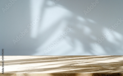 Table shadow background. Wooden table and white empty wall with plant shadows.