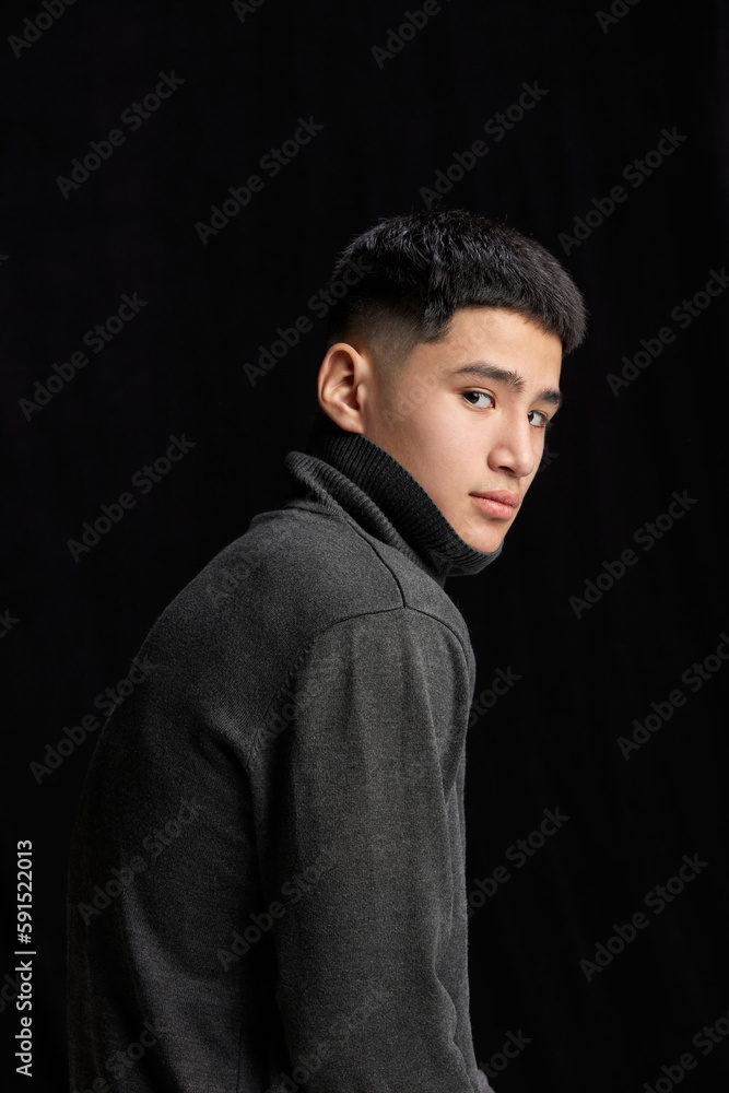 Portrait of handsome young guy in stylish black jumper, turtleneck, point against dark studio background. Modern style. Concept of fashion, body aesthetics, beauty, men's health, emotions Portrait of handsome young guy in stylish black jumper, turtleneck, point against dark studio background. Modern style. Concept of fashion, body aesthetics, beauty, men's health, emotions