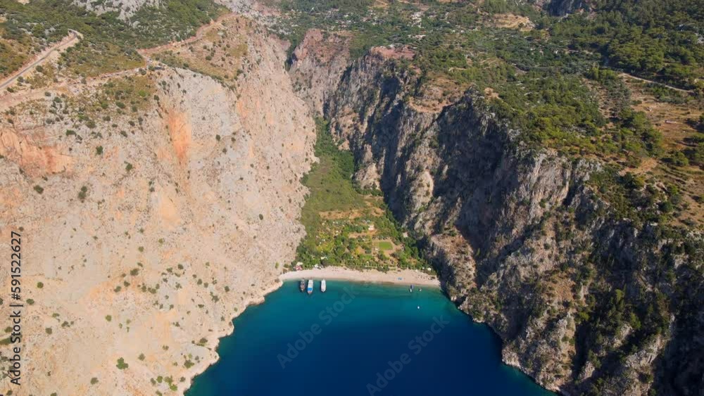 Drone video capturing the pristine Butterfly Valley in Ölüdeniz, Fethiye, featuring its tranquil beach, canyon, waterfall, and boats cruising along the vibrant turquoise sea. Drone video capturing the pristine Butterfly Valley in Ölüdeniz, Fethiye, featuring its tranquil beach, canyon, waterfall, and boats cruising along the vibrant turquoise sea.