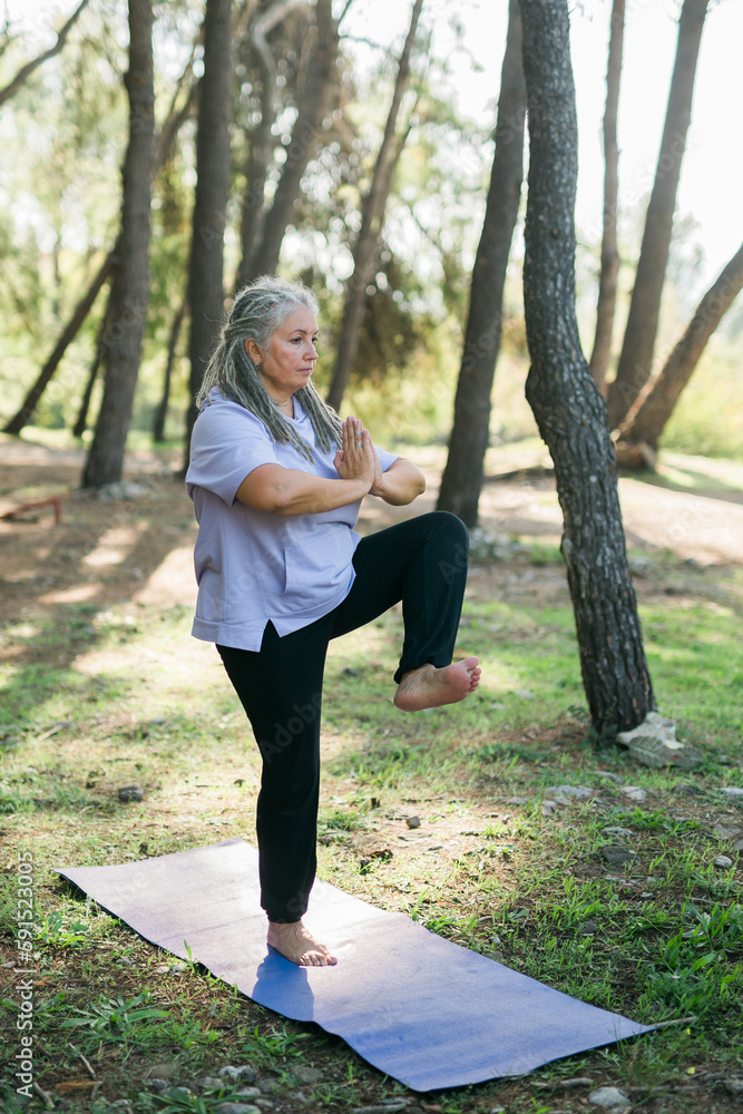 Mature elderly grey haired dreadlocks woman training in park, doing yoga or fitness - wellbeing and healthy lifestyle concept