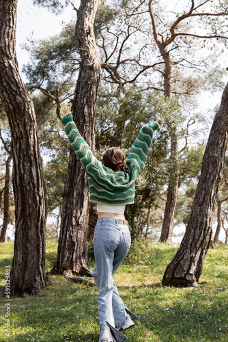 Back view of brunette woman in sweater and jeans walking in summer park.