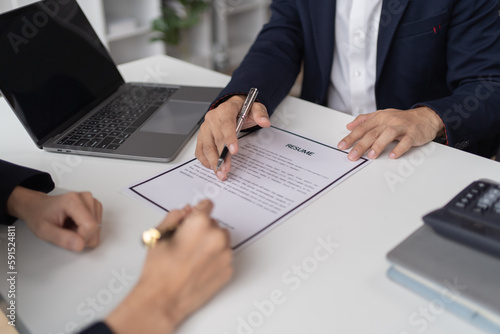 Happy young Asian businessman and woman shaking hands to congratulate successful collaboration on business deal with documents and laptop on table in the office.