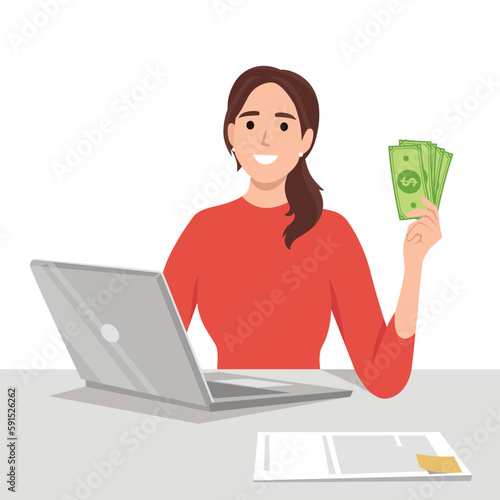 Successful businesswoman with green banknote money fan making thumbs up gesture sitting on office desk with laptop