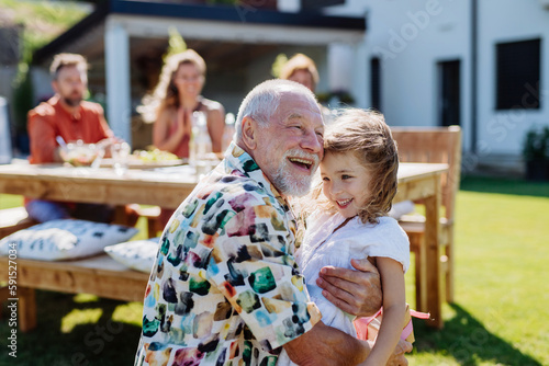 Happy little girl giving birthday present to her senior grandfather at generation family birthday party in summer garden photo