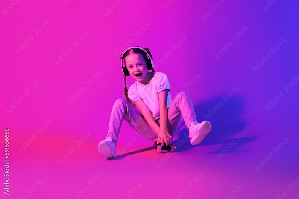 Emotional cute school-aged girl posing with skateboard on studio background Emotional cute school-aged girl posing with skateboard on studio background