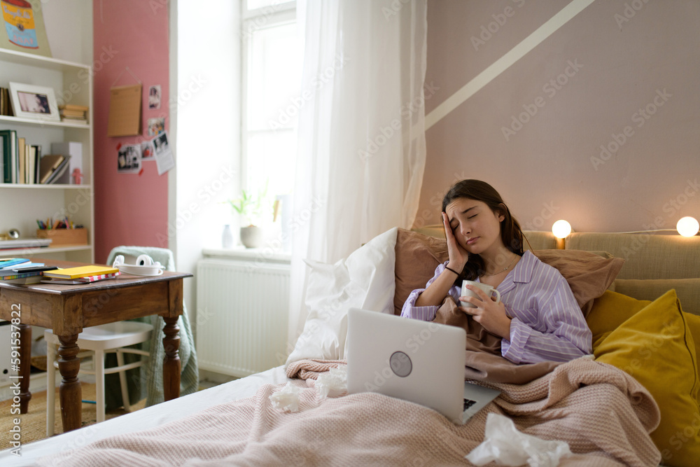 Sick teenage girl laying in her bed with laptop. Sick teenage girl laying in her bed with laptop.