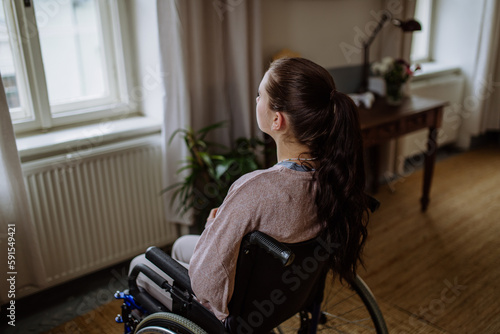 Unhappy teenage girl sitting on a wheelchair and looking out of the window.