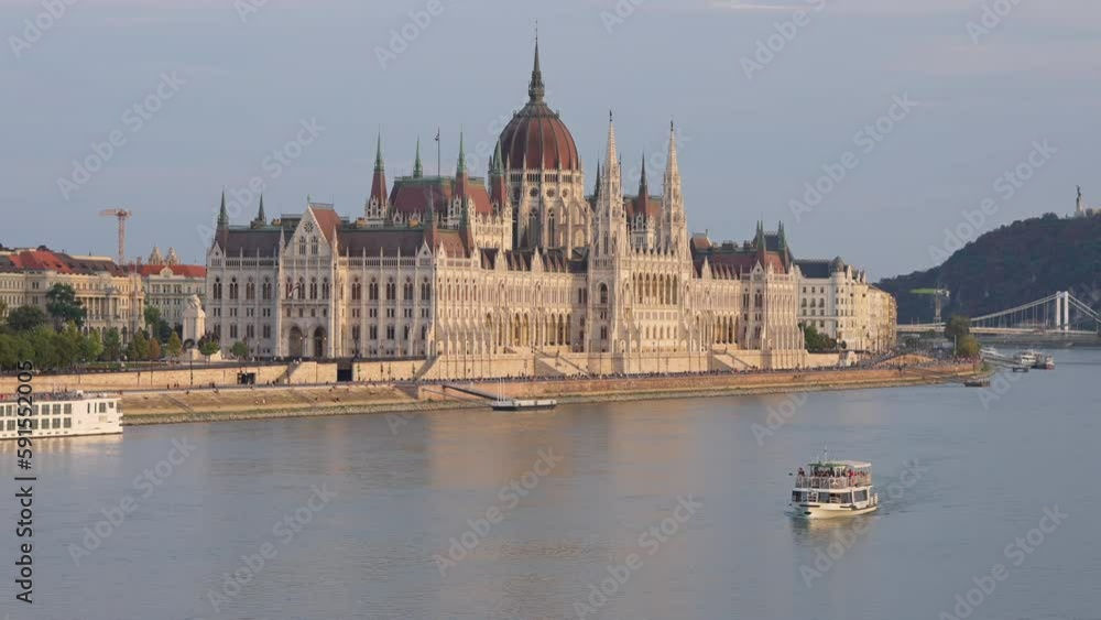 Wide shot building with ferry on river in sunshine. Gothic style ancient city building and ship on water in sunslight on spring day Wide shot building with ferry on river in sunshine. Gothic style ancient city building and ship on water in sunslight on spring day